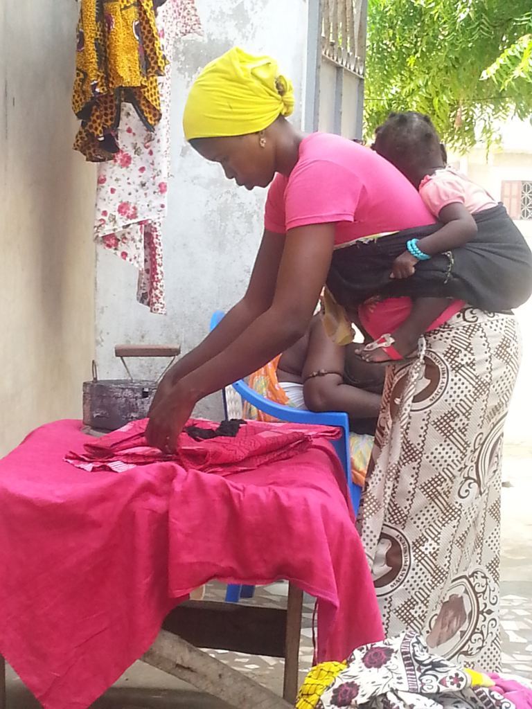So sieht der Alltag in Dakar aus. Das Kind auf den Rücken und die Kleidung mit altem Bügeleisen bügeln.